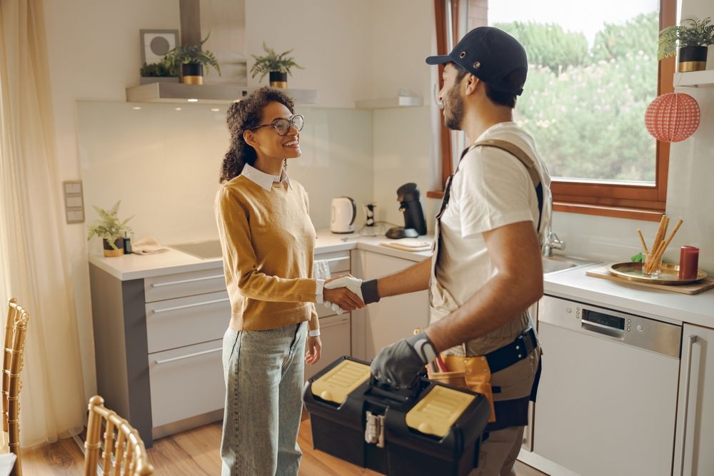 A homeowner shaking hands with a plumber in her kitchen