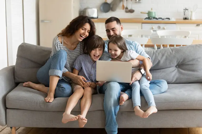 A happy family sitting on a couch using a laptop to support the Hampton Roads Home Services mission