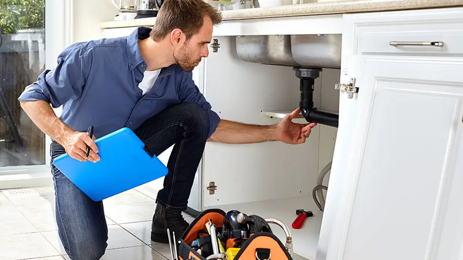Professional plumber inspecting pipes under a kitchen sink in Hampton Roads home